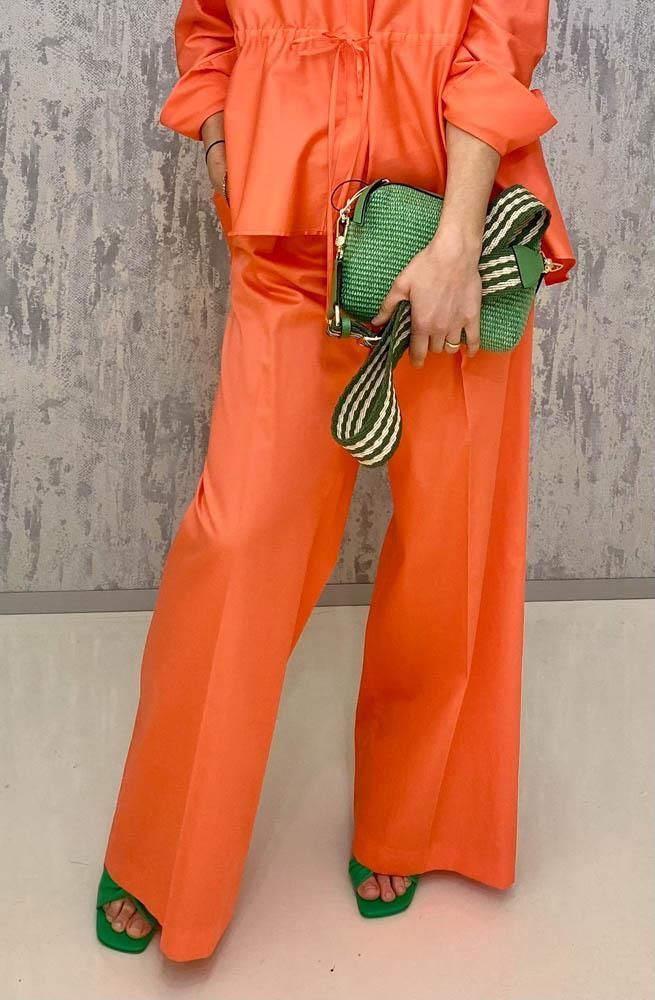 Eine Frau in orangefarbenen Hosen und grünen Schuhen hält eine grüne Tasche