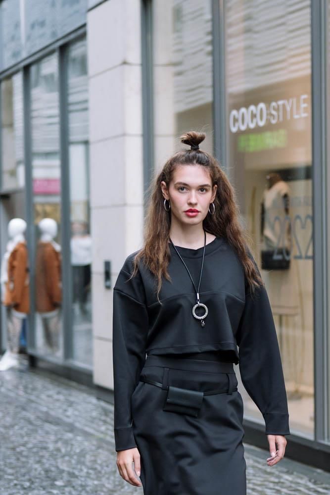 Eine Frau mit einem schwarzen Pullover und einem schwarzen Rock steht vor einem Geschäft.
