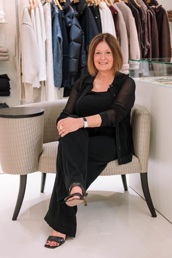 Eine Frau sitzt auf einem Stuhl vor einem Kleiderständer.