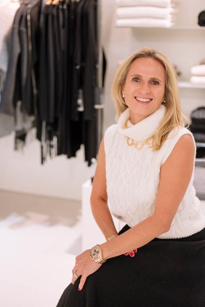 Eine Frau mit einem weißen Pullover und einem schwarzen Rock sitzt in einem Geschäft auf einem Hocker.