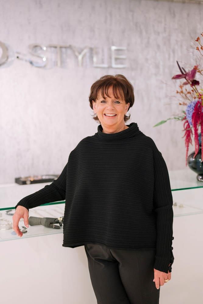 Eine Frau in einem schwarzen Pullover steht vor einer Theke.