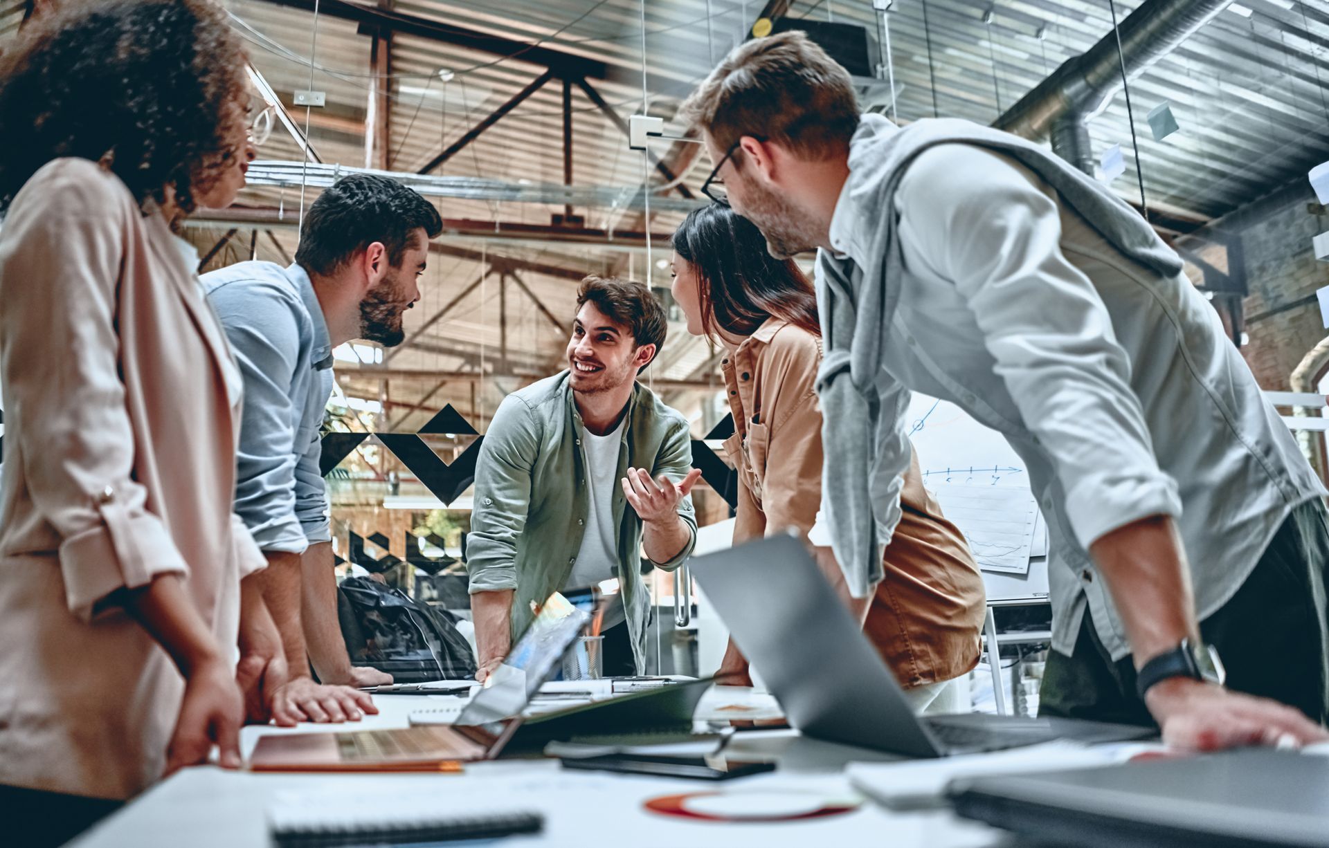 Réunion d'équipe dans un bureau industriel lumineux ; les gens sont penchés sur une table et discutent de leur travail.