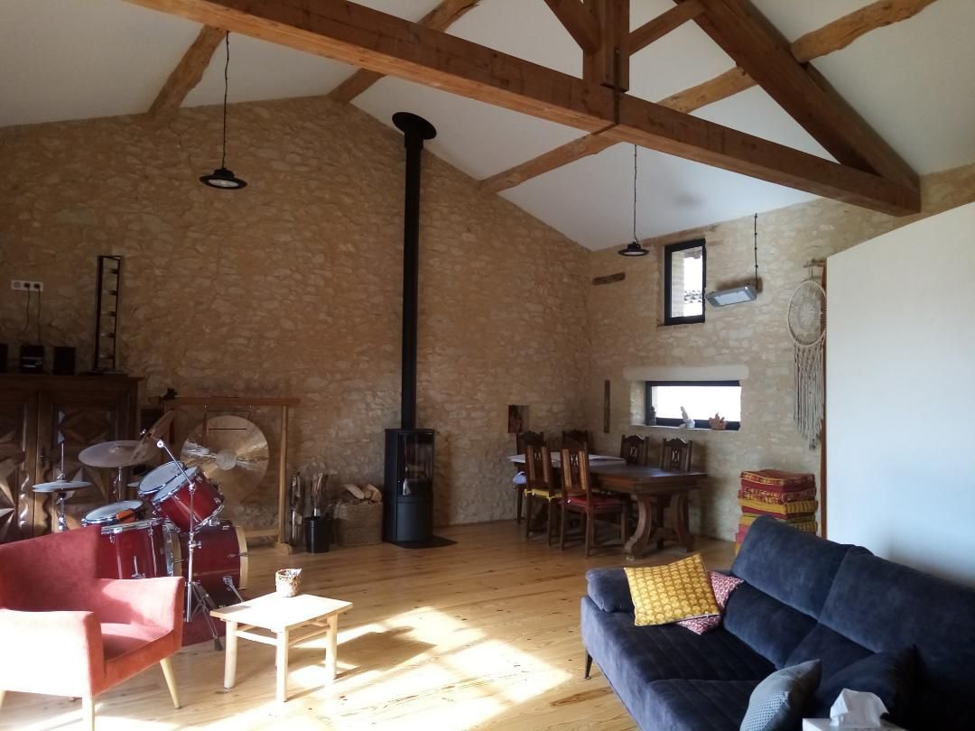 Salon rustique de style loft avec poutres apparentes, mur de briques, canapé noir, poêle à bois et table à manger.