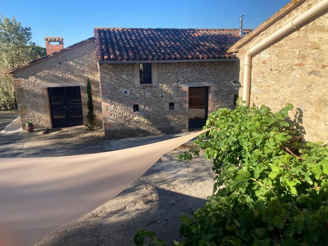 Maison en pierre dans une rue tranquille d'un village, avec un toit de tuiles et des buissons verts au premier plan.