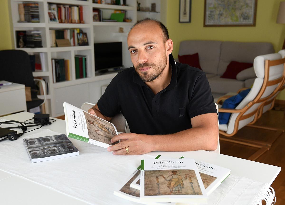 Una persona está sentada a una mesa blanca sosteniendo un libro con un mosaico de estilo romano en la portada, con varios ejemplares sobre la mesa.