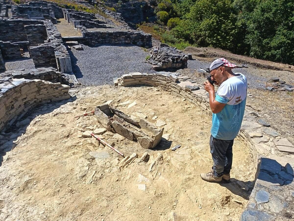 Yacimiento de Chao Samartín (Grandas de Salime) Persona fotografiando un yacimiento de ruinas de piedra en un día soleado.