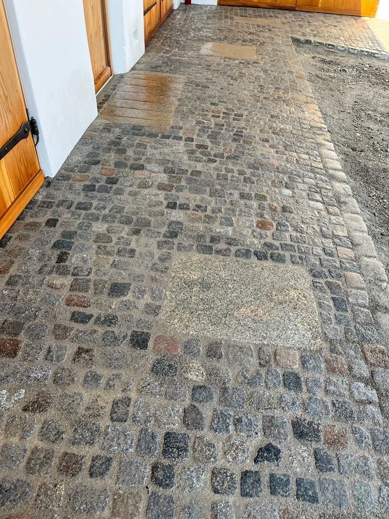 Ein Kopfsteinpflasterweg führt zu einem Gebäude mit einer Holztür.