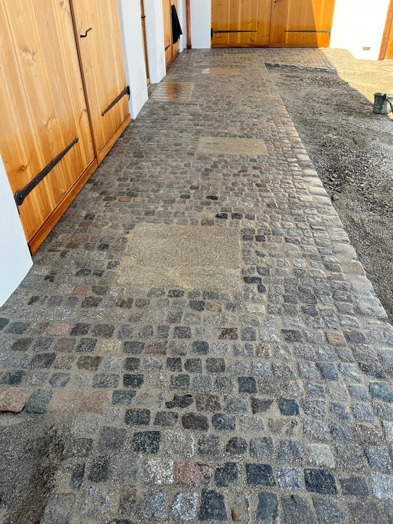 Ein Kopfsteinpflasterweg führt zu einer Garage mit Holztüren.