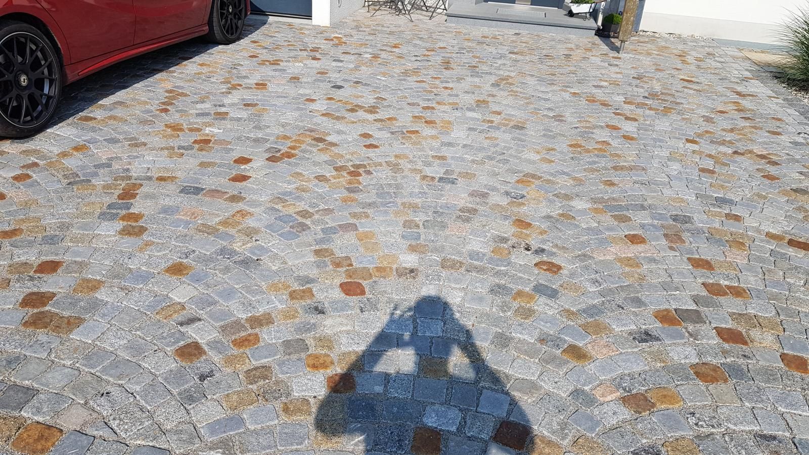 Ein rotes Auto ist in einer Einfahrt geparkt. Auf dem Boden liegt der Schatten einer Person.