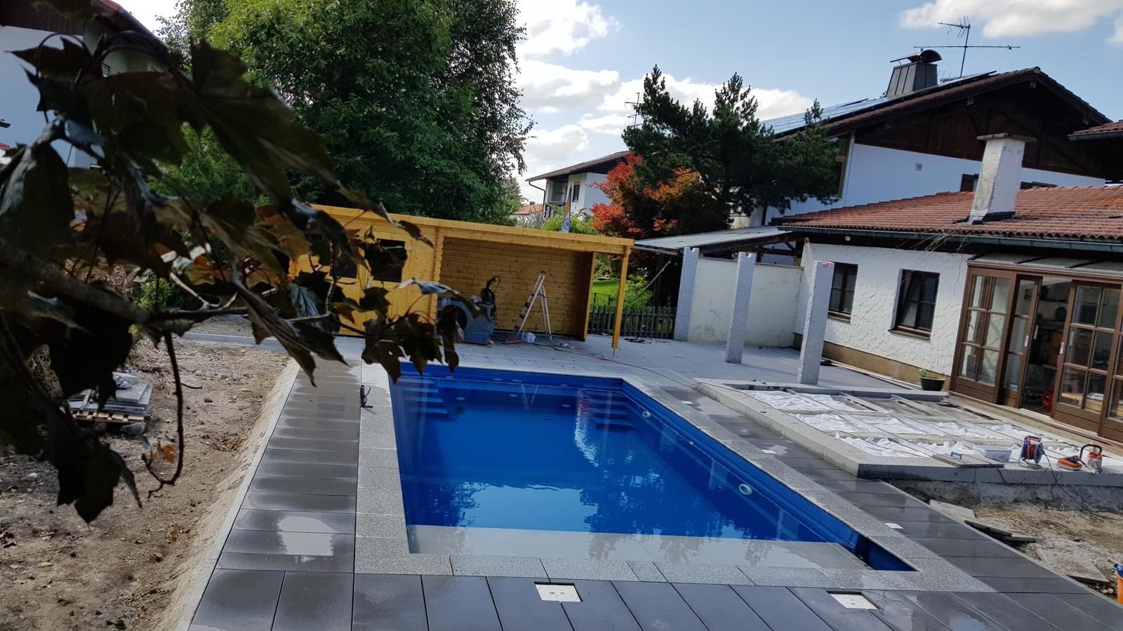 Im Hinterhof eines Hauses wird ein großes Schwimmbecken gebaut.