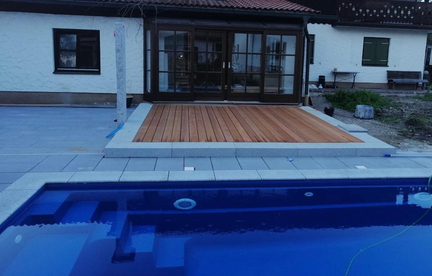 Ein Swimmingpool mit Holzdeck vor einem Haus.