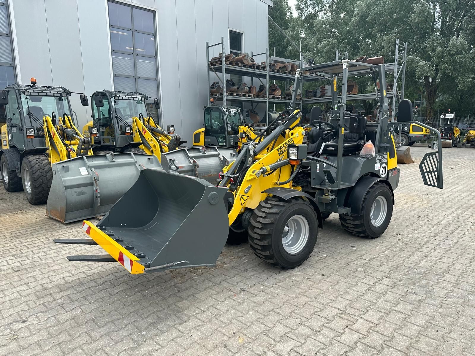 Eine Reihe gelber und grauer Traktoren parkt vor einem Gebäude.