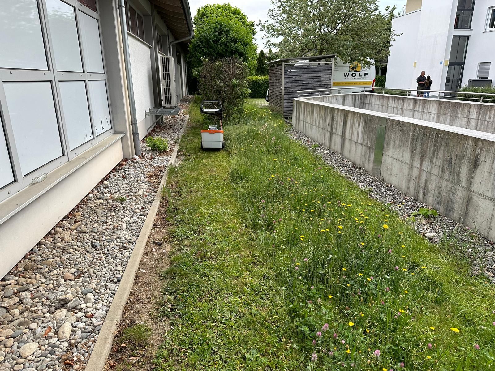 Ein Rasenmäher steht im Gras neben einem Gebäude.