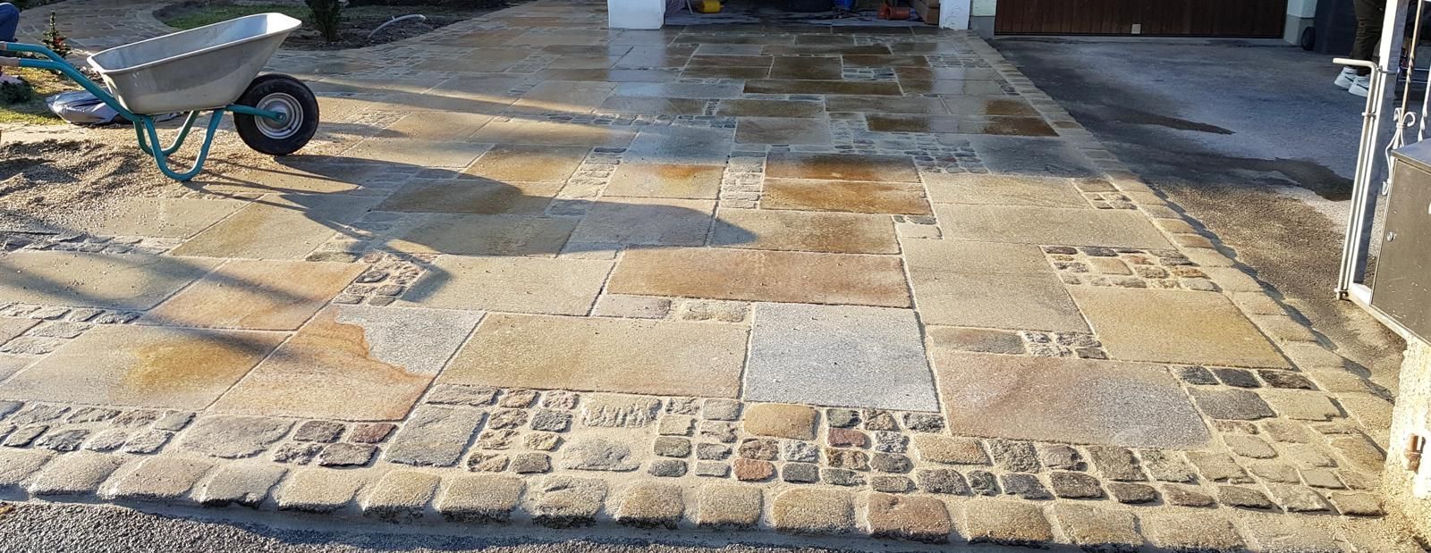 Eine Schubkarre steht am Rand einer gepflasterten Auffahrt.