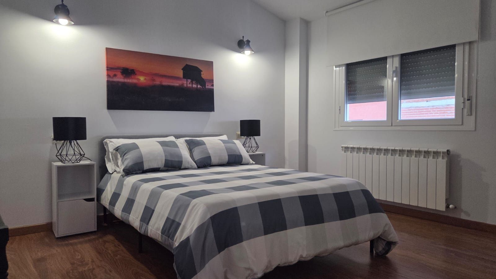 Un dormitorio con una cama tamaño queen cubierta con un edredón a cuadros grises y blancos, dos mesitas de noche 