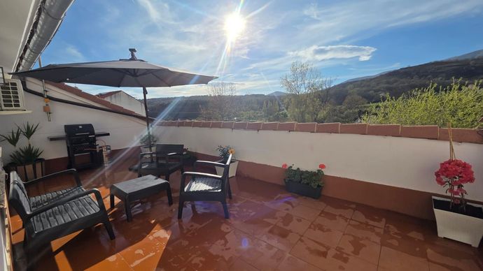 Una terraza soleada al aire libre con muebles de exterior oscuros, una sombrilla