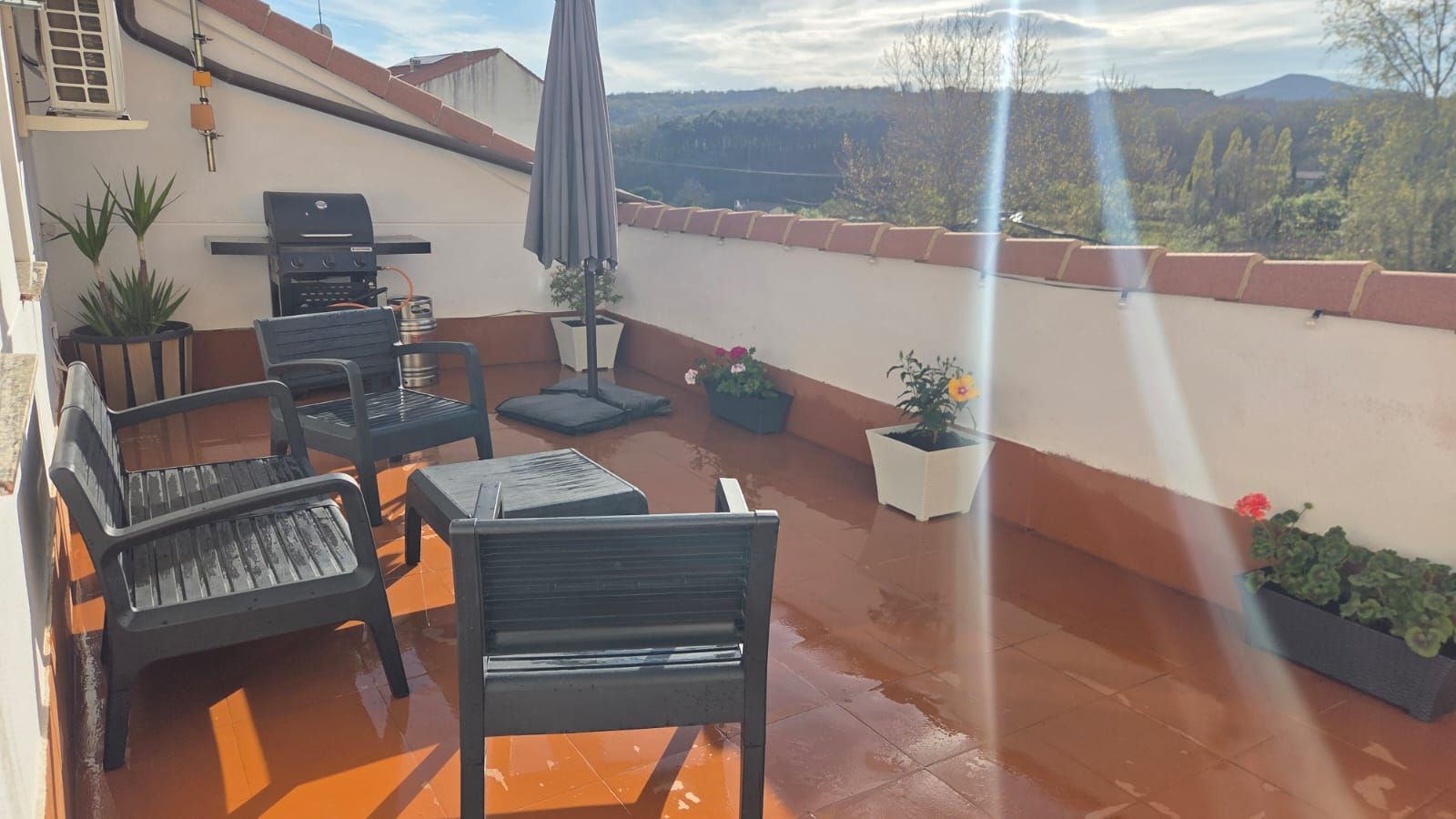 Un balcón con sillas oscuras de exterior, una mesa pequeña, una parrilla, una sombrilla cerrada