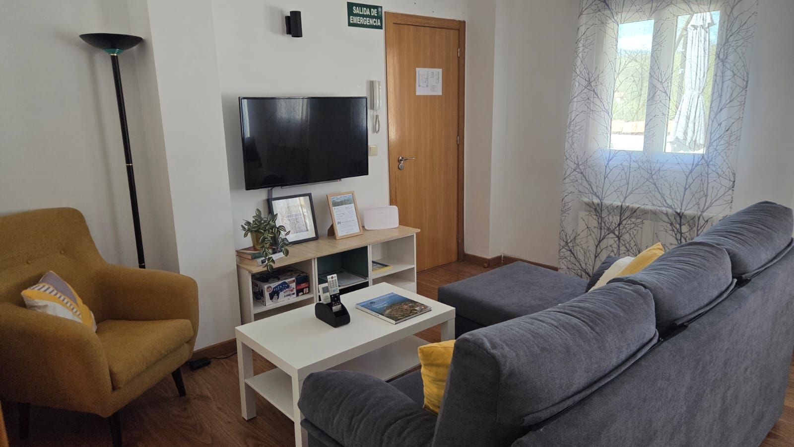 Una acogedora sala de estar con un sillón amarillo mostaza, un sofá gris, una mesa de centro blanca