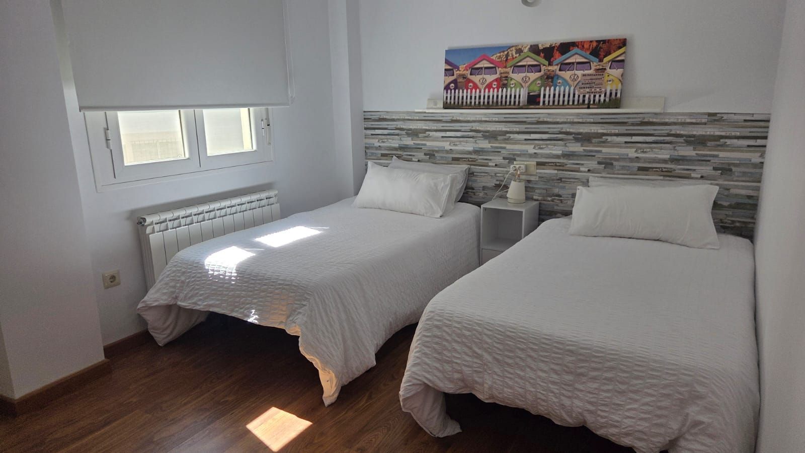 Un dormitorio con dos camas individuales una al lado de la otra, ropa de cama blanca, cabecero de pared 