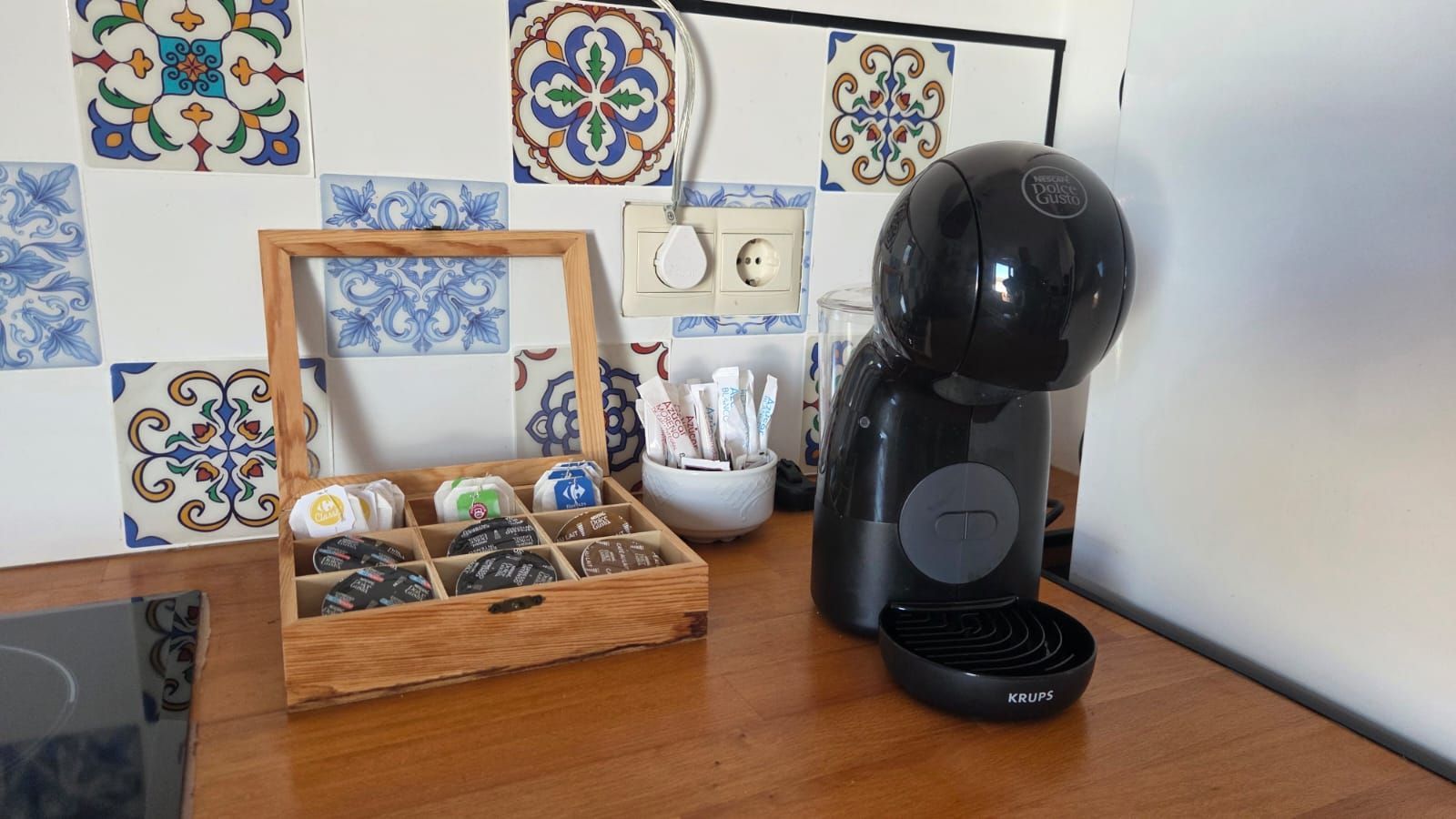 Una cafetera negra, una caja de madera con cápsulas de café y un recipiente con edulcorantes 