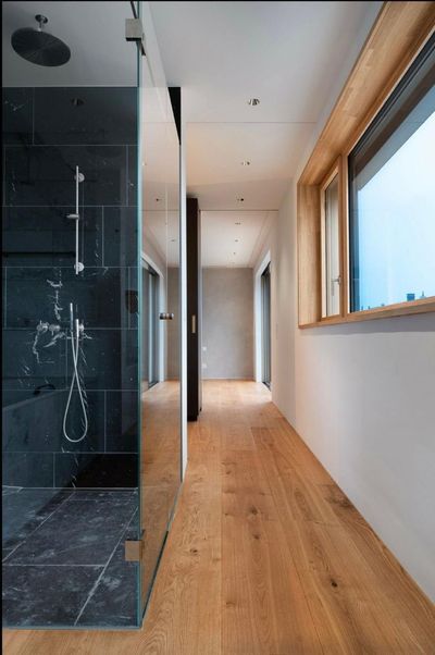 Moderner Flur mit Holzboden, weissen Wänden, grossen Fenstern und einer schwarzen Glasduschkabine auf der linken Seite.