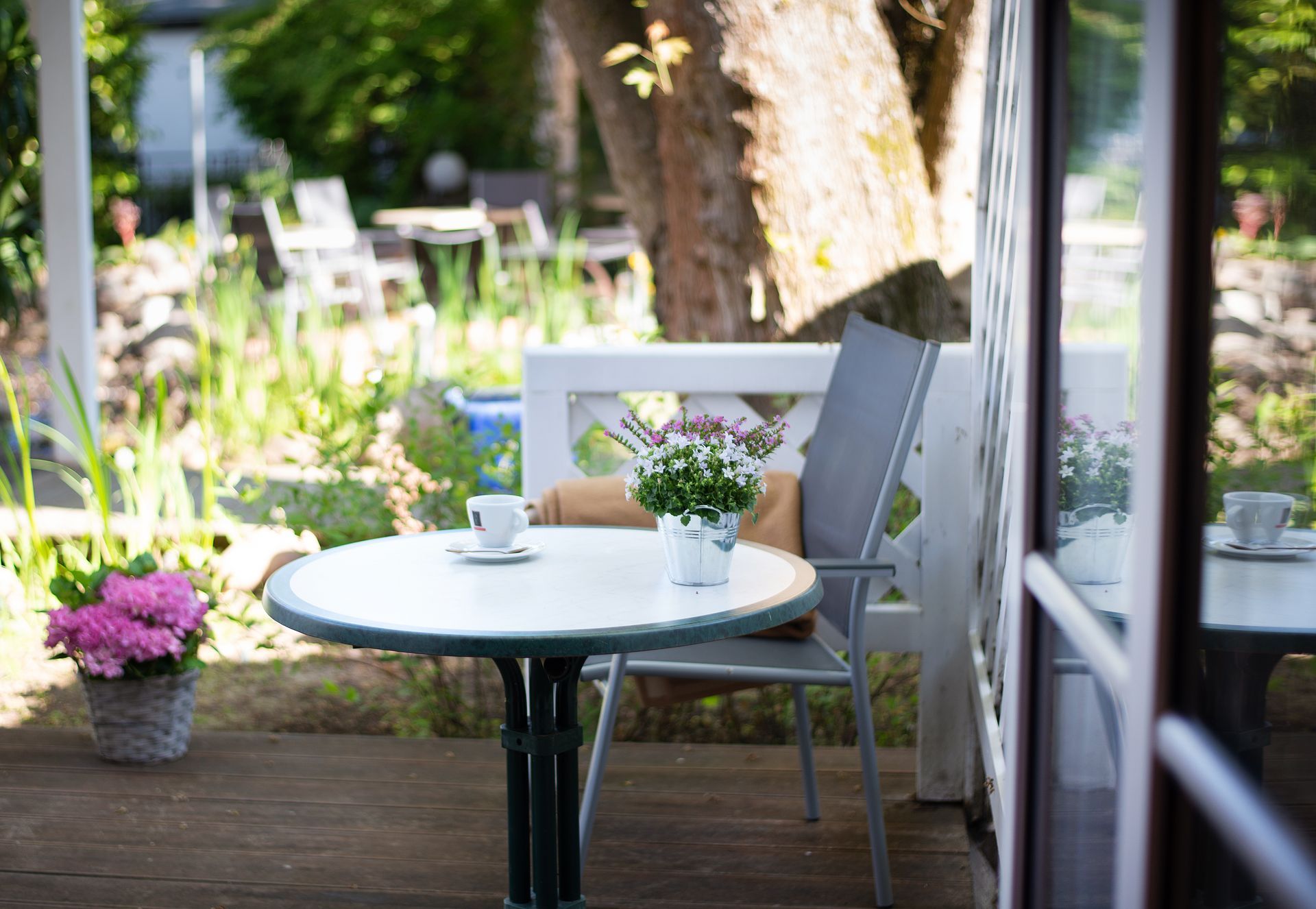 Terrasse mit gedecktem Tisch für Tee, Topfblumen, Stuhl, Gartenhintergrund.
