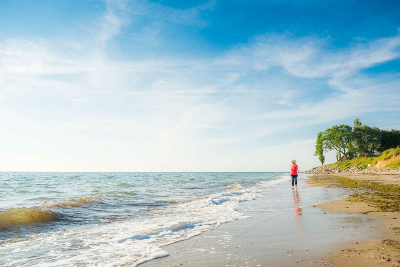 Frau geht in Rot unter einem blauen Himmel mit Wolken an einem Strand spazieren.