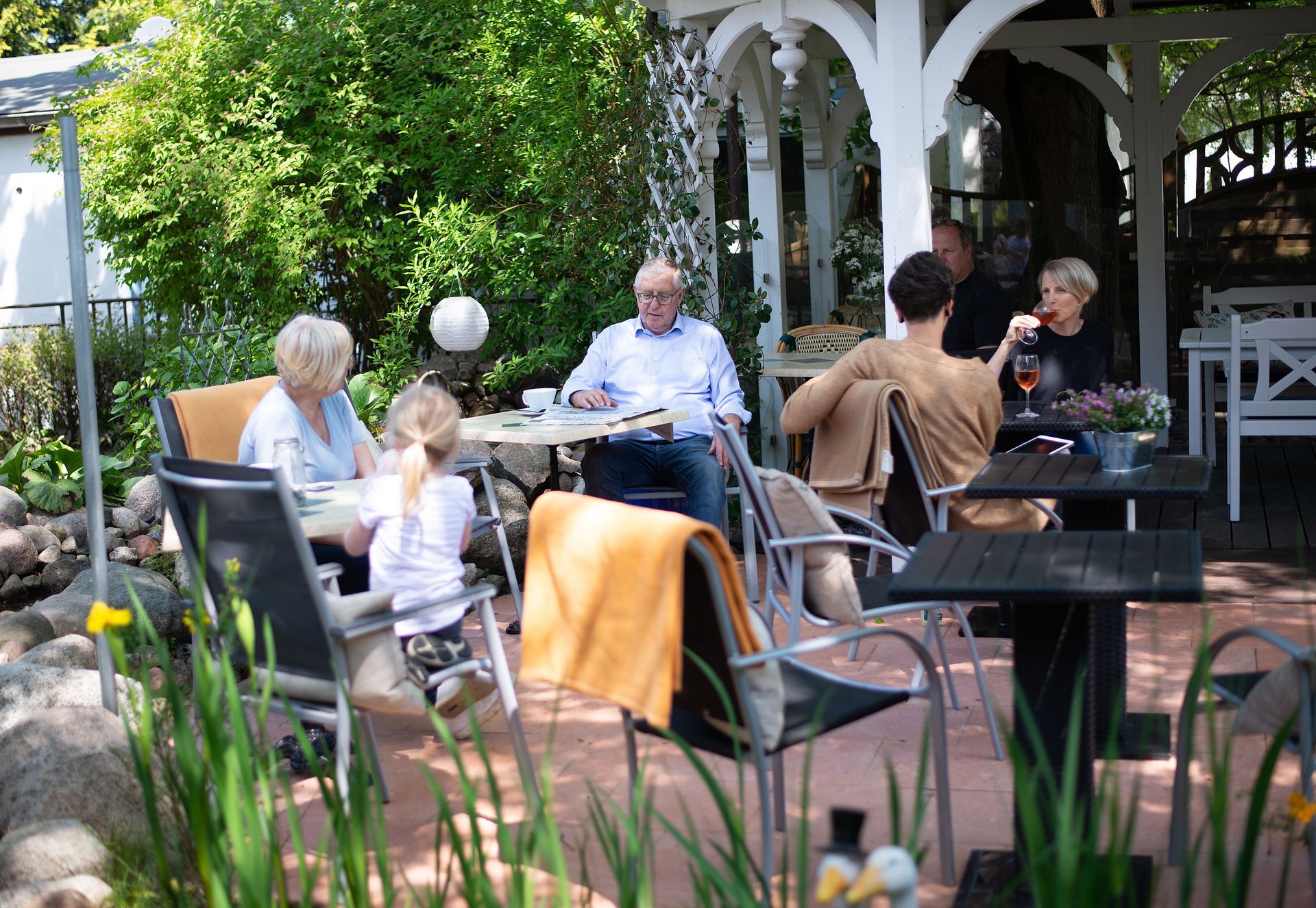 Menschen unterhalten sich im wunderschönen Hotel Garten unter freiem Himmel, umgeben von weißen Bögen und viel Grün.