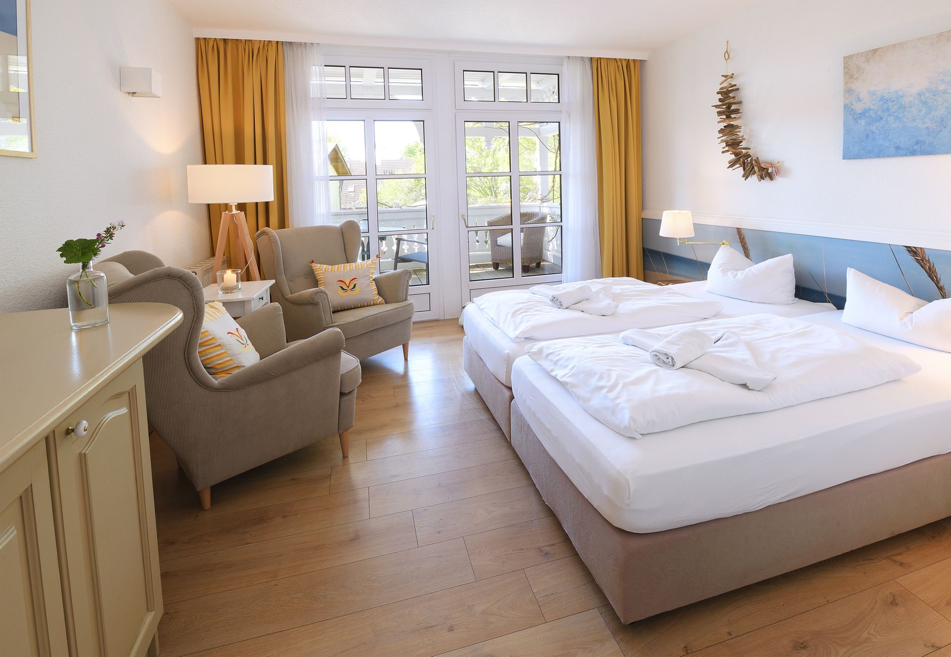 Helles Schlafzimmer mit zwei Betten, Sesseln, Flügeltüren und warmem Tageslicht