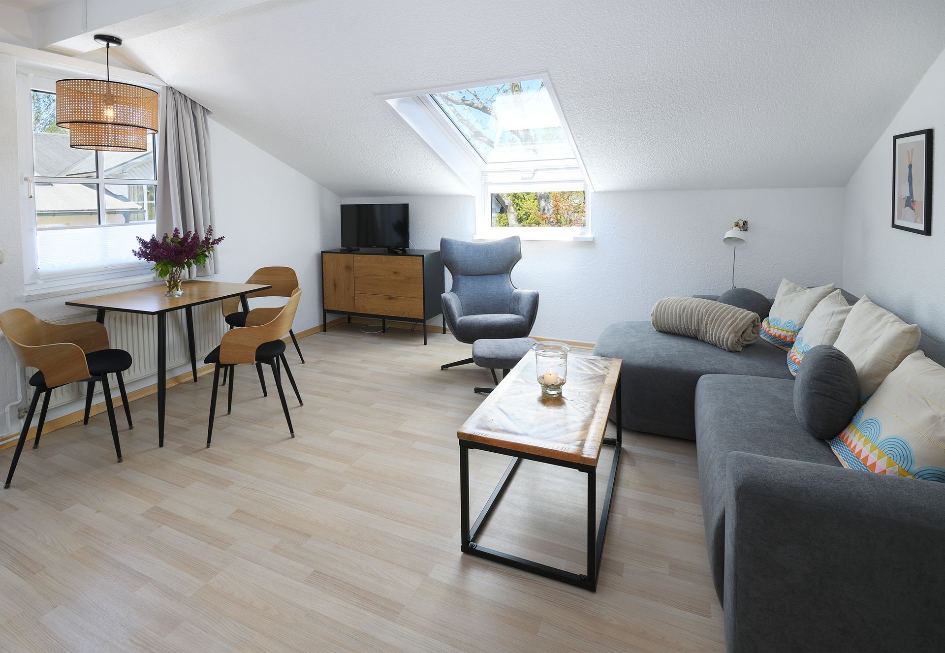 Helles, modernes Wohnzimmer mit grauer Eckcouch, Couchtisch, Essbereich, Fernseher und Dachfenster
