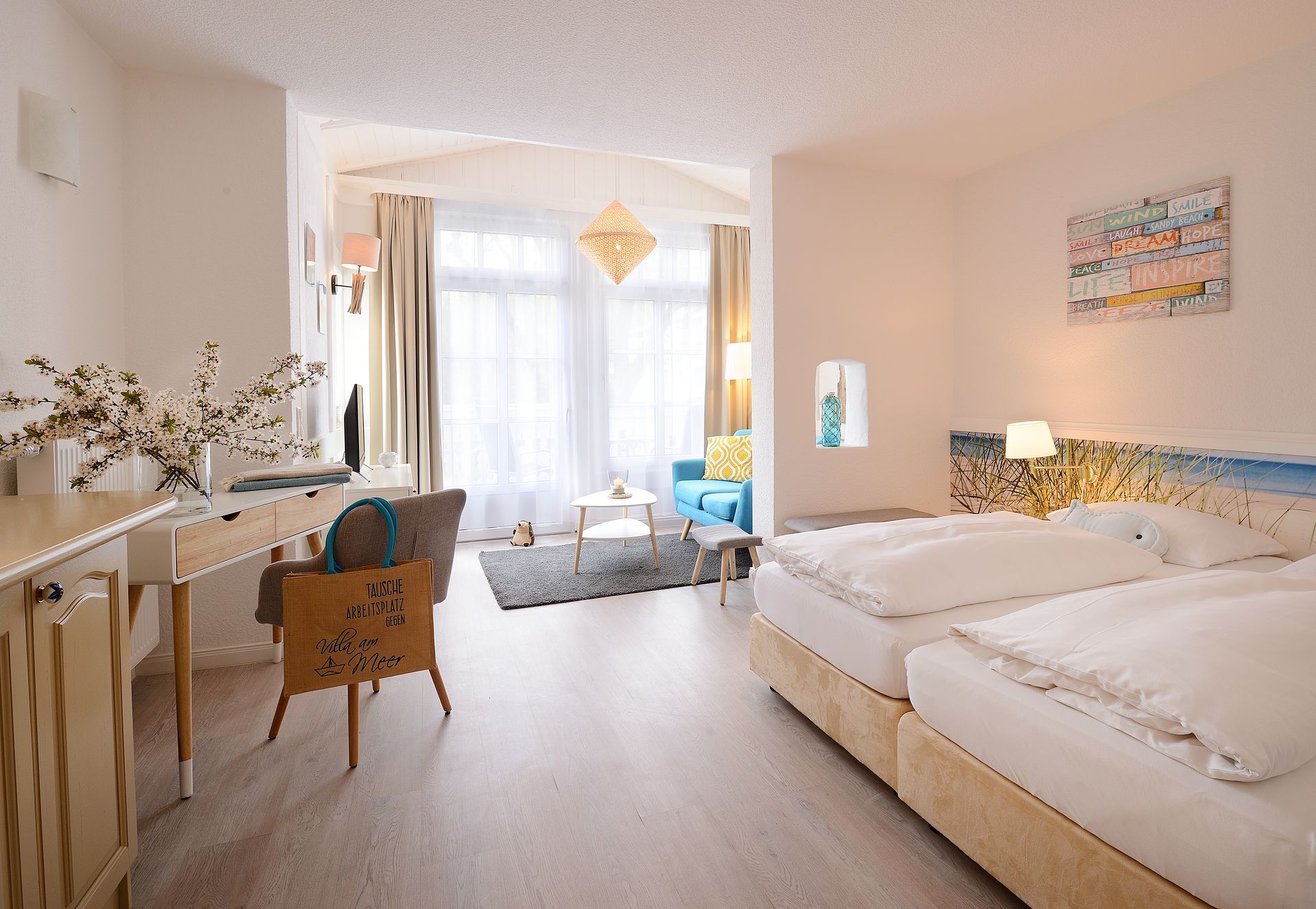 Helles Hotelzimmer mit zwei Einzelbetten, Schreibtisch, Sitzecke und großen Fenstern.