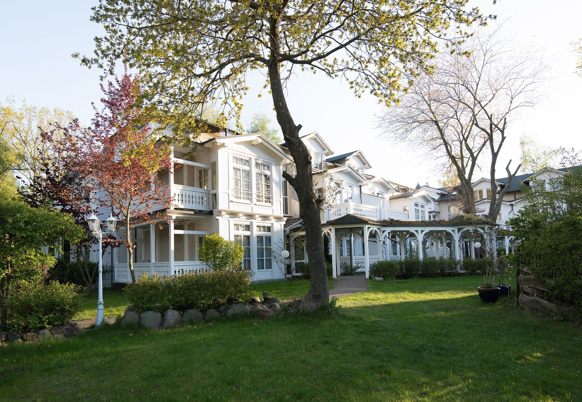Haus im Bäderstil bekannt an der Ostsee mit Veranda und blühenden Bäumen neben einem grünen Rasen an einem sonnigen Tag