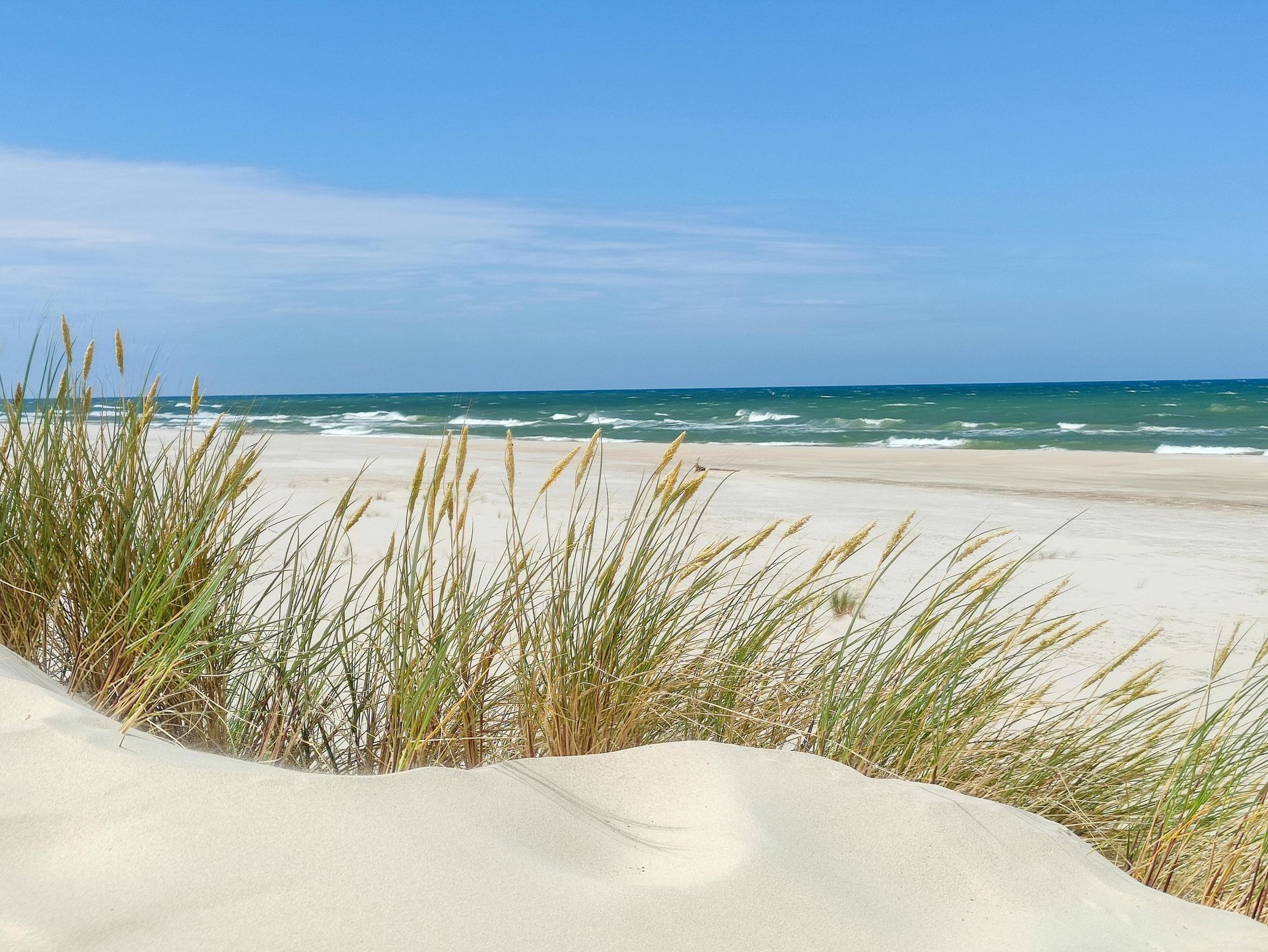 Sonnenstrand mit weißen Sanddünen, hohem Gras und türkisfarbenem Meer unter blauem Himmel