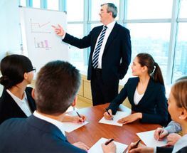 Un hombre está dando una presentación a un grupo de empresarios sentados alrededor de una mesa.