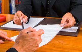 Dos personas están sentadas en una mesa firmando un documento.