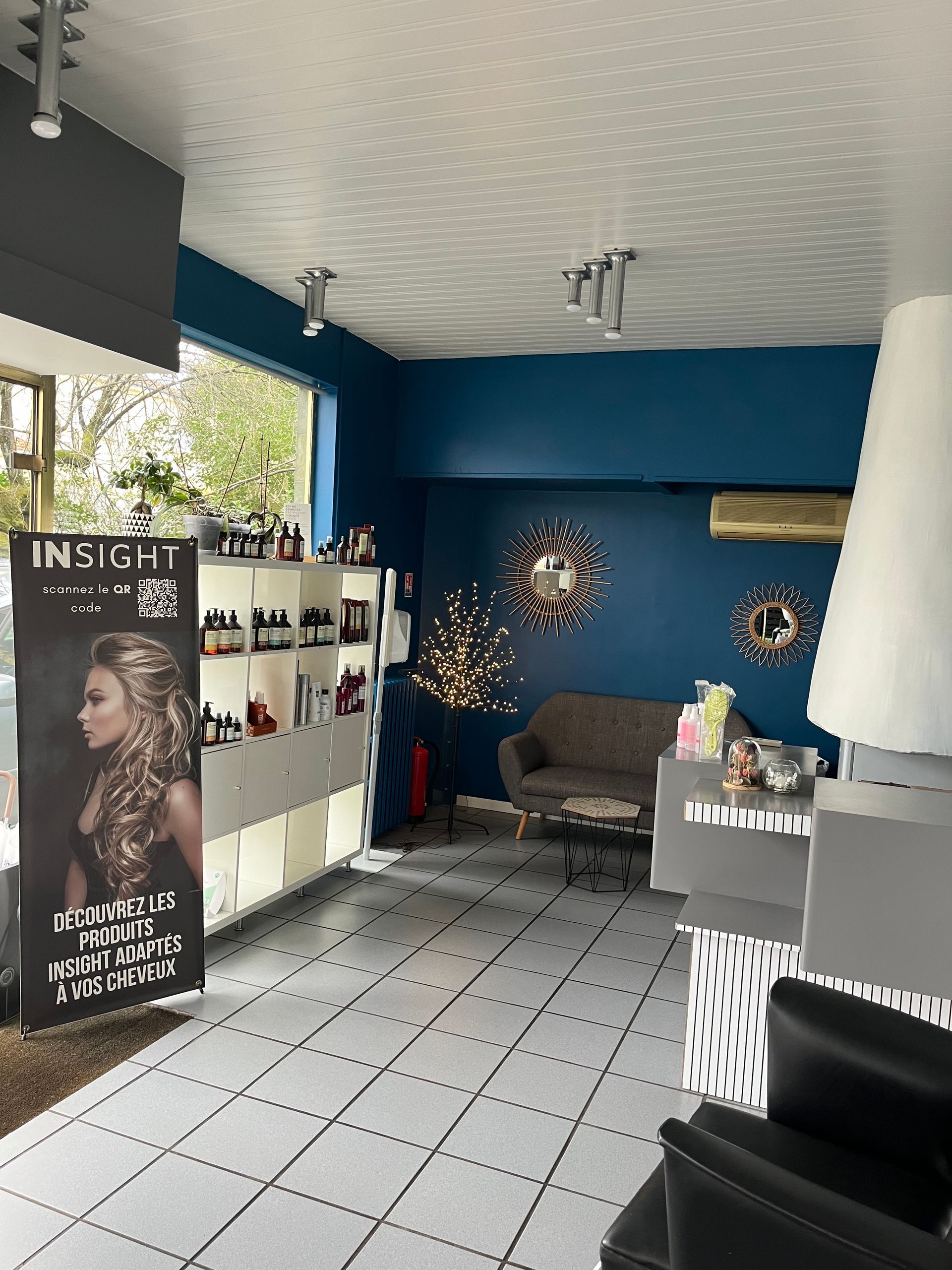 Intérieur du salon de coiffure, vue sur la vitrine, publicité Insight, murs bleus avec miroirs et canapé gris