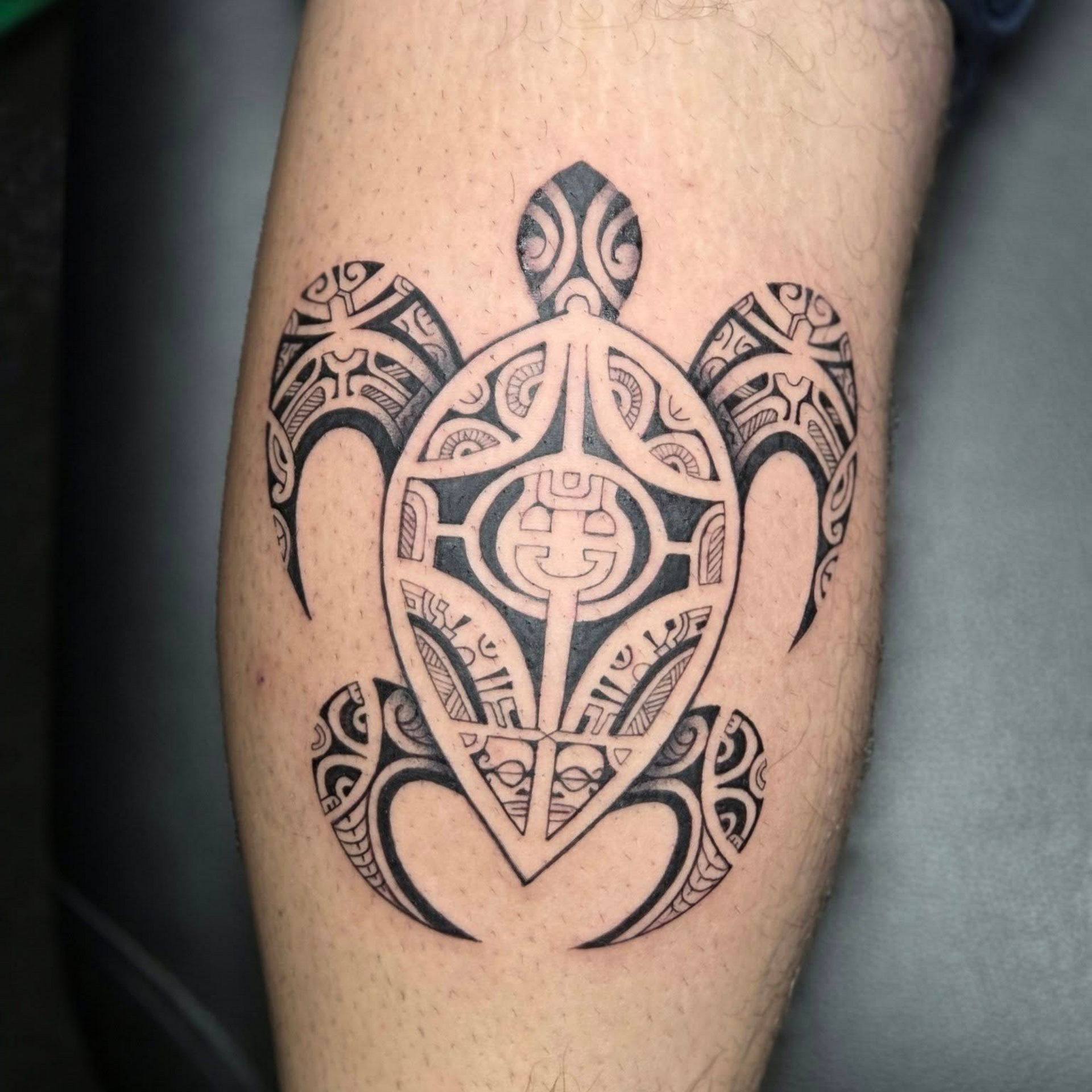 Bras tatoué dans un style polynésien traditionnel, avec des motifs géométriques noirs complexes sur l'épaule et l'avant-bras.
