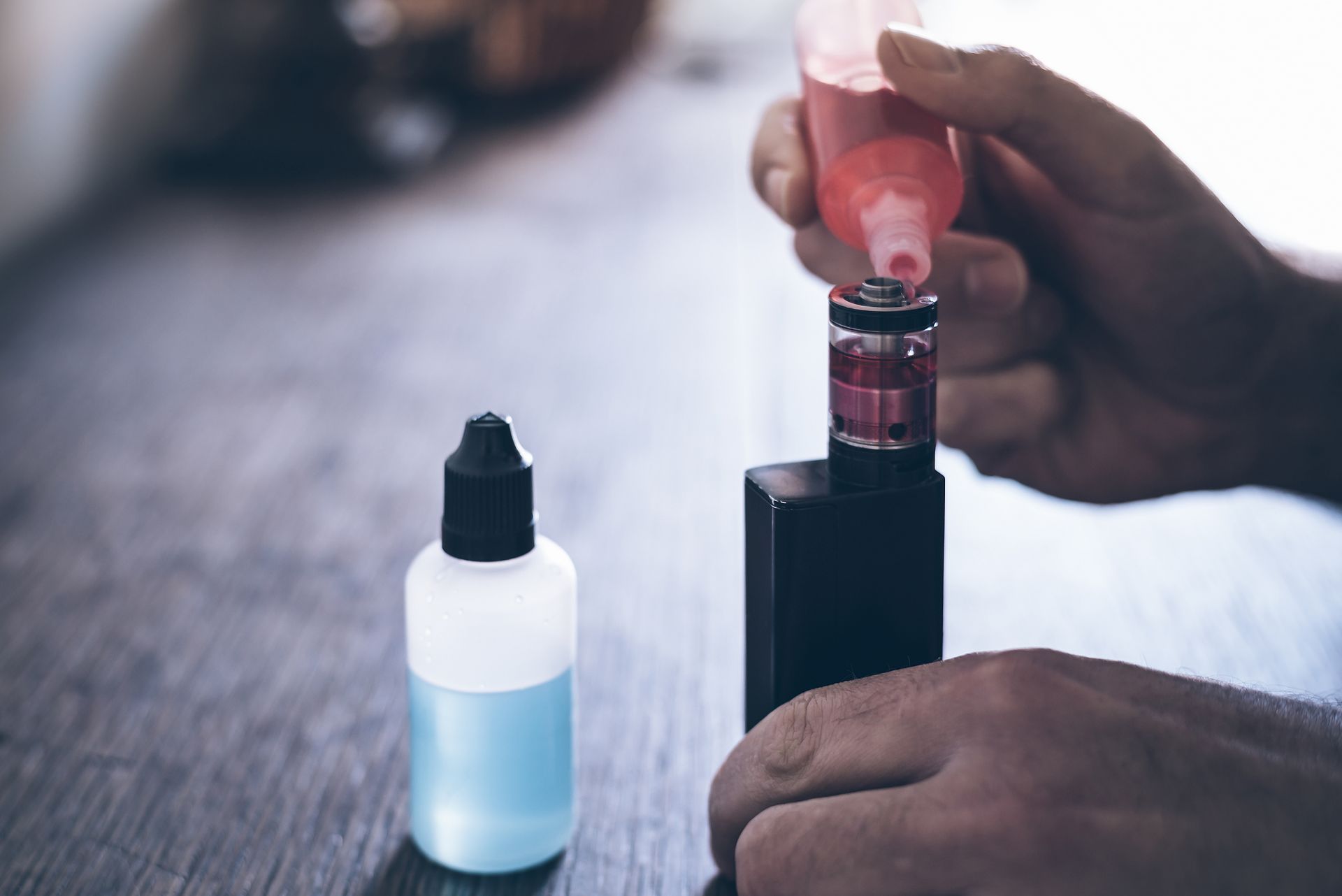 Personne remplissant un appareil de vapotage avec du e-liquide rose à partir d'une bouteille sur une table en bois.