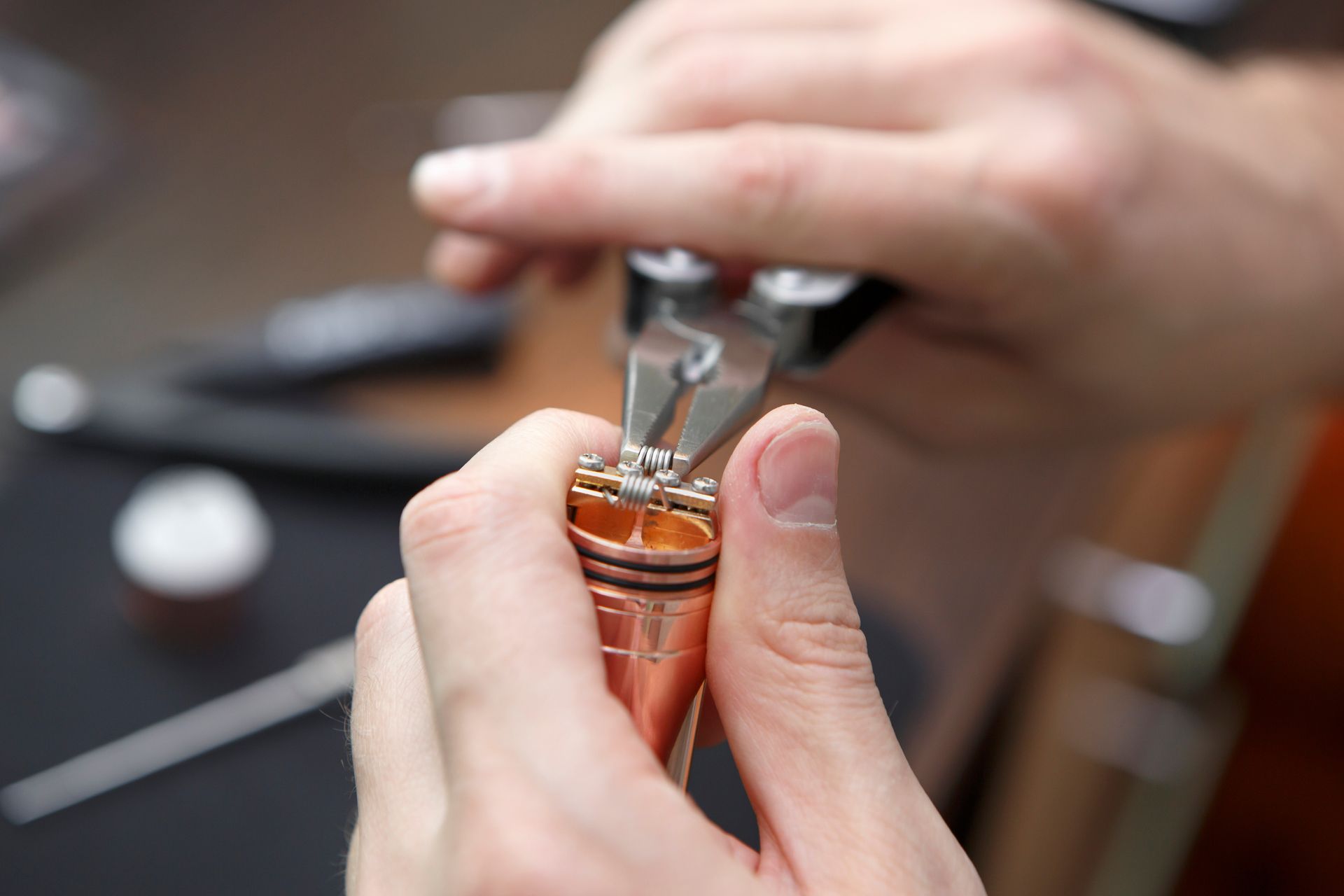 Mains utilisant des pinces pour manipuler un petit objet en cuivre, probablement destiné à la fabrication de bijoux.