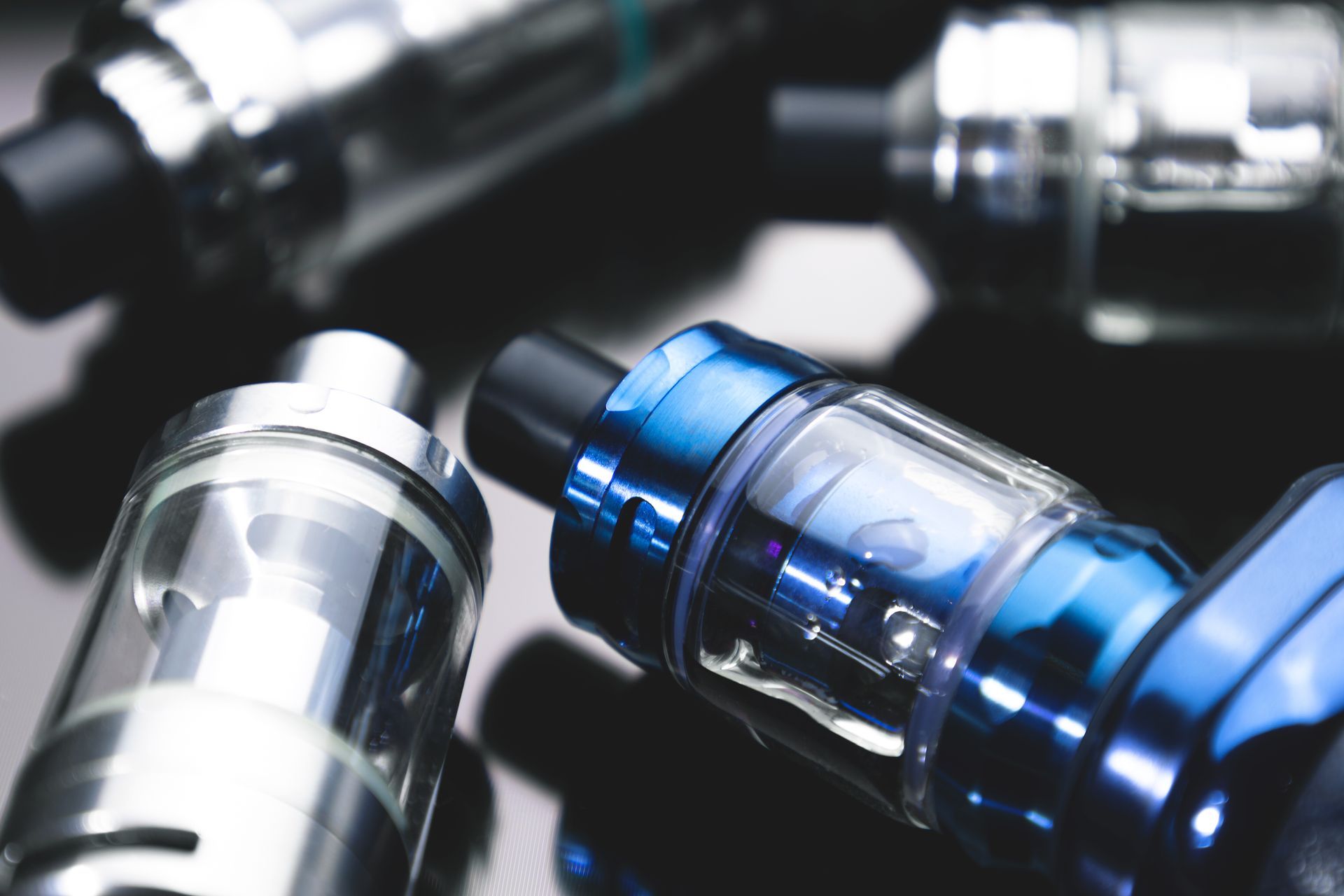 Gros plan de plusieurs stylos vape brillants sur une surface sombre réfléchissante, certains avec des accents bleus.
