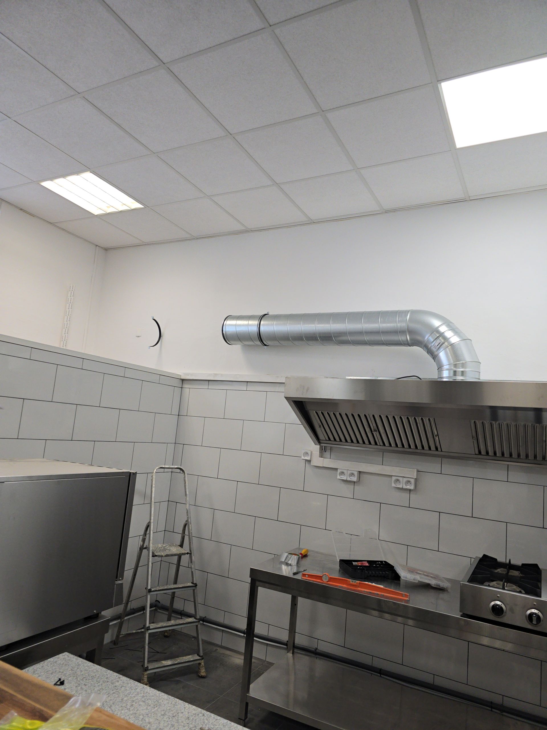 Cuisine professionnelle équipée d'appareils en acier inoxydable, d'une hotte aspirante, d'une échelle et de murs carrelés sous éclairage fluorescent.