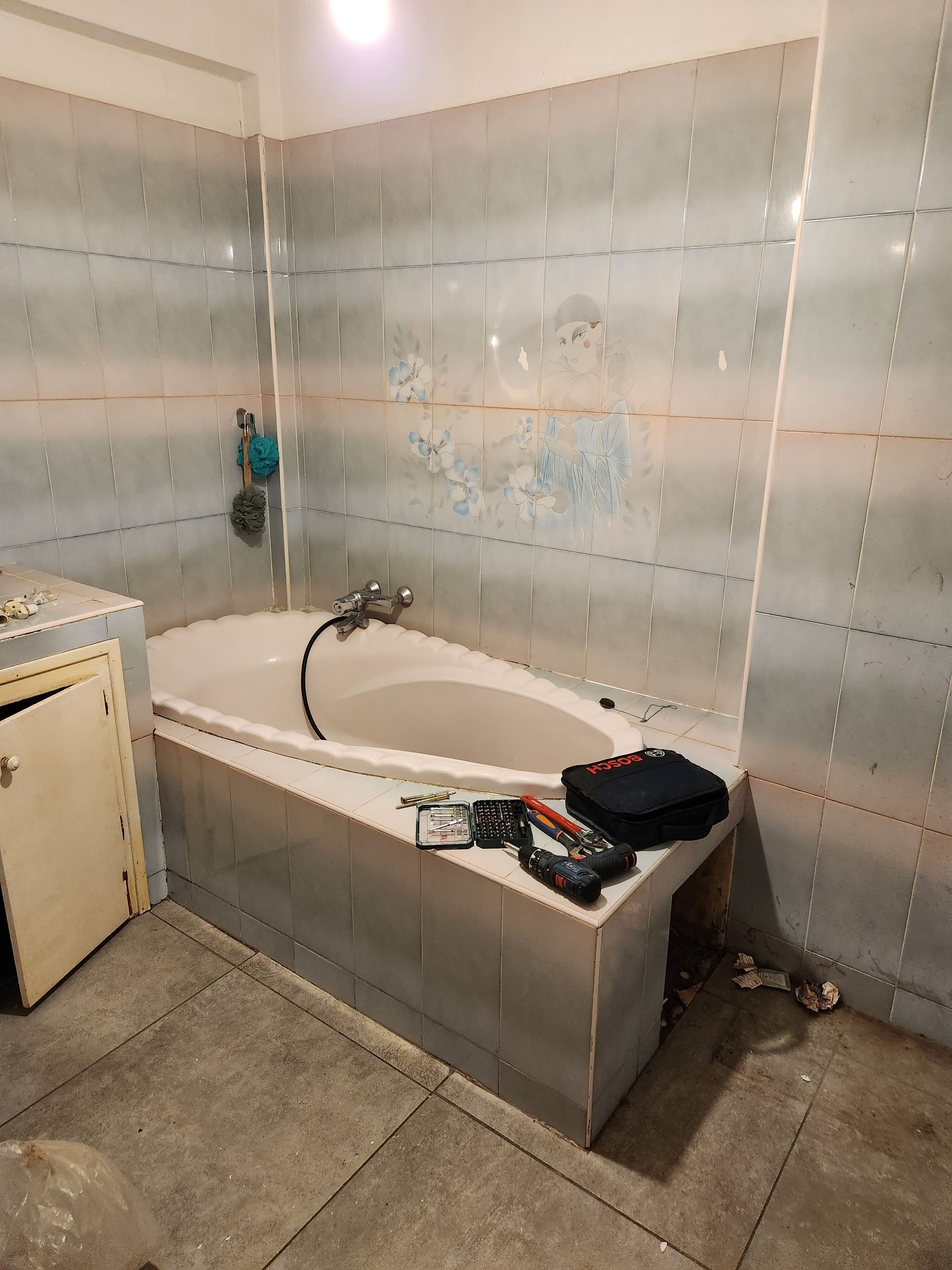Salle de bains avec baignoire, murs carrelés et produits de nettoyage sur le rebord de la baignoire.