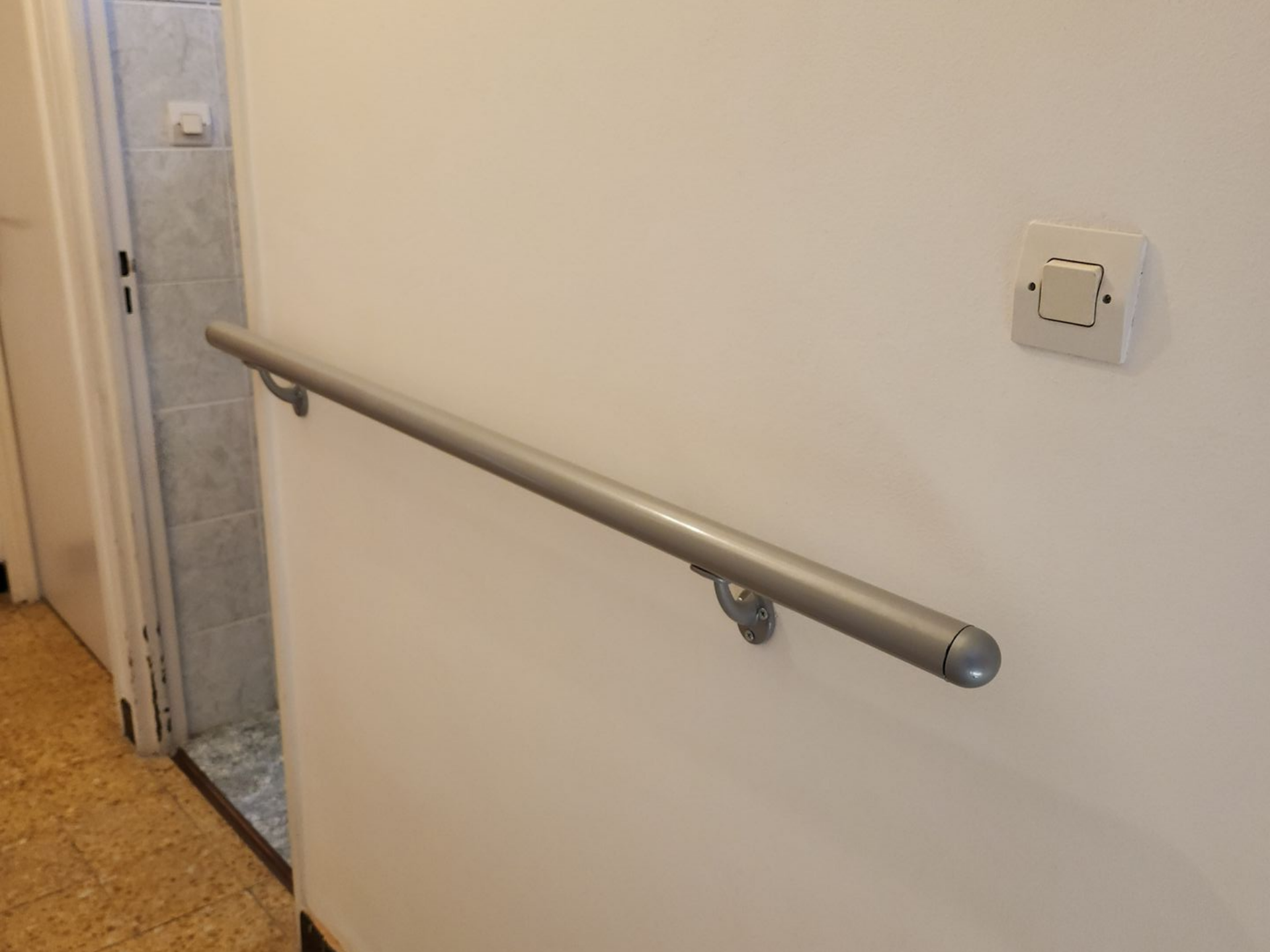 Mur blanc dans le couloir avec une rampe argentée fixée à côté d'une porte.
