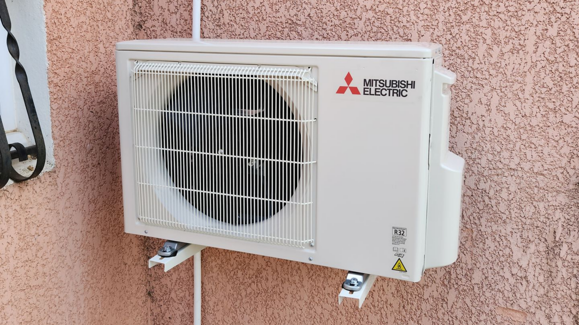 Climatiseur Mitsubishi Electric blanc, monté sur un mur extérieur en stuc rose.
