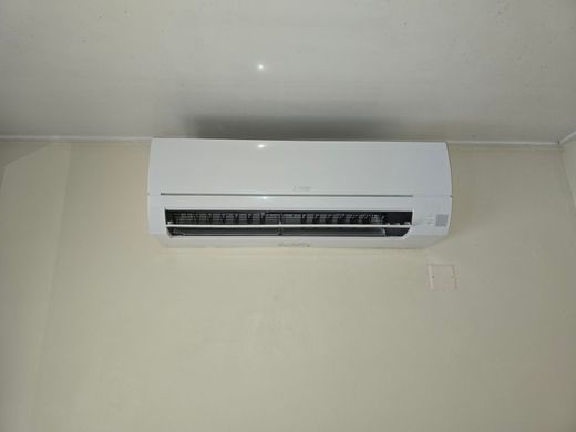 Climatiseur mural blanc, fixé sur un mur intérieur uni, centré près du plafond.