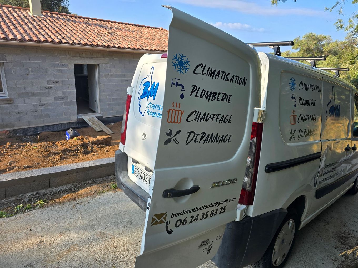 Camionnette de livraison blanche avec des panneaux publicitaires garée à côté d'un bâtiment en pierre dans une rue ensoleillée.