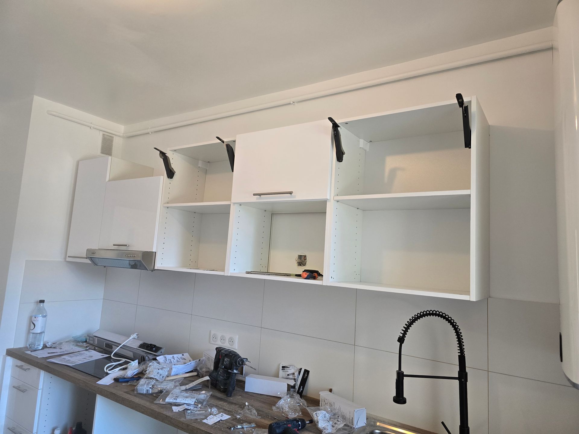 Cuisine blanche avec placards hauts ouverts et contenu visible, évier en dessous et outils de rénovation sur le plan de travail.