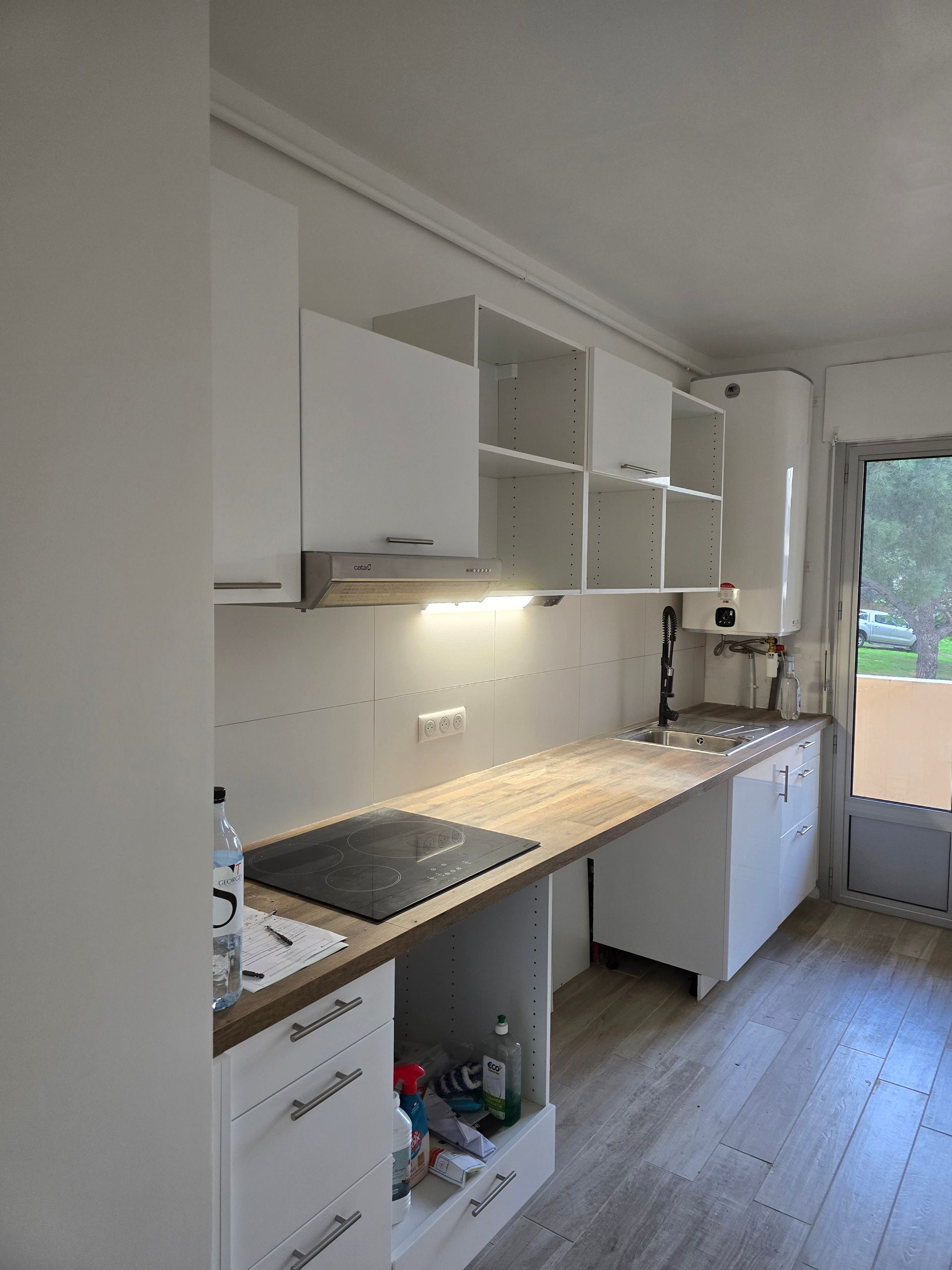 Cuisine en longueur, d'un blanc éclatant, avec placards, plan de travail, évier et fenêtre près d'une porte.