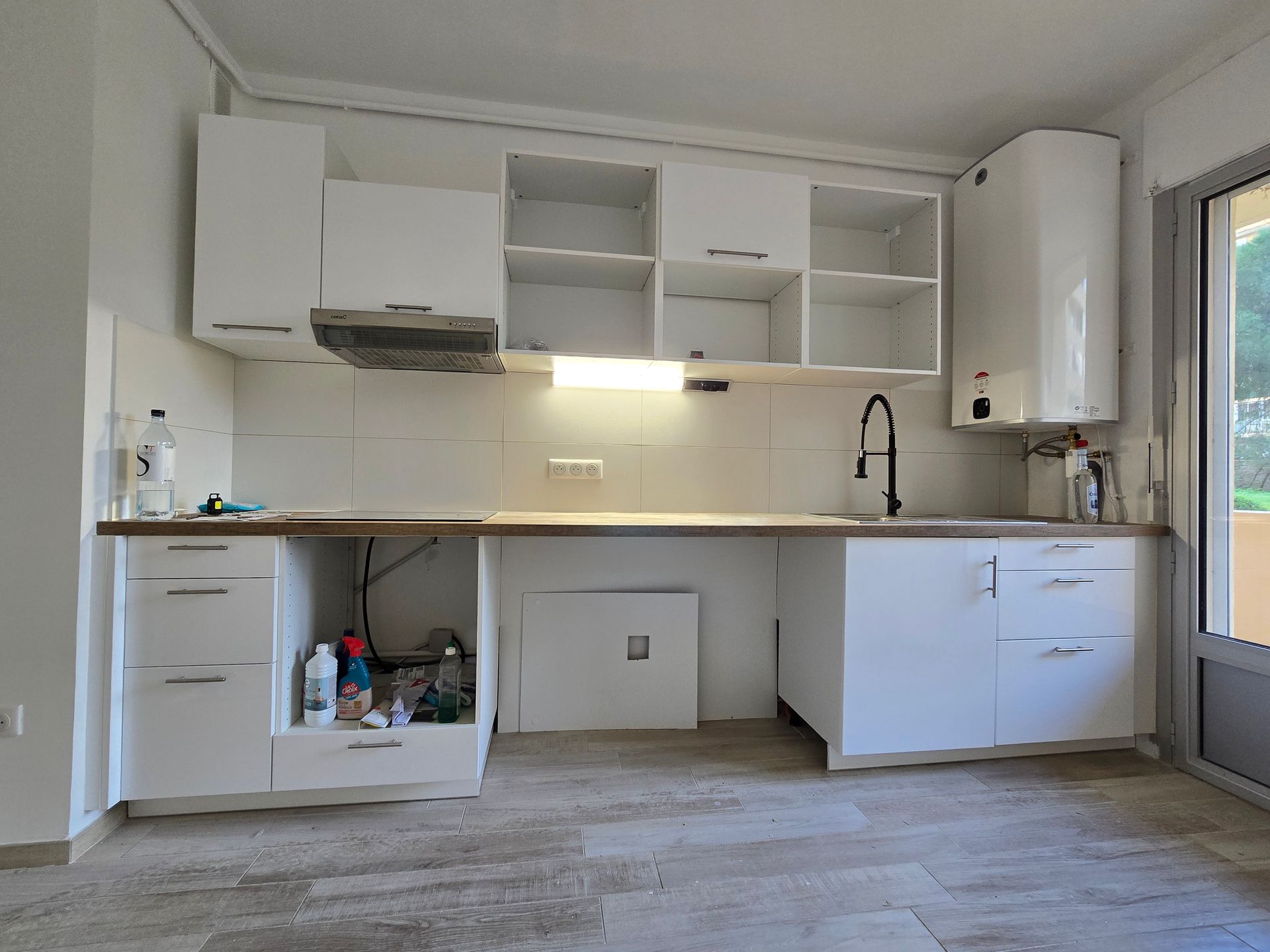 Cuisine moderne et lumineuse avec placards blancs, comptoirs en bois, évier et grandes fenêtres.