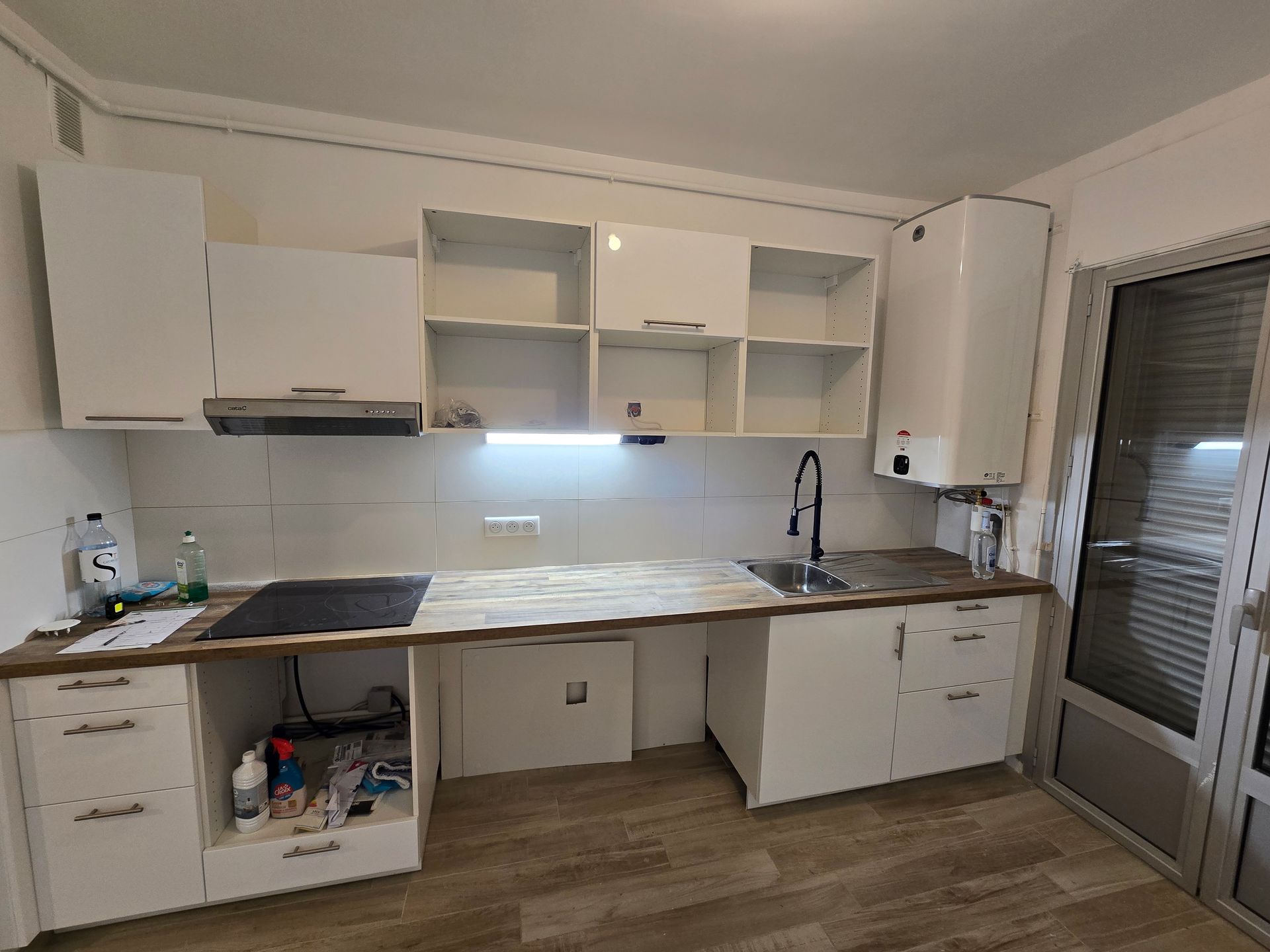 Cuisine moderne avec placards blancs, comptoirs imitation marbre et porte vitrée sur la droite.